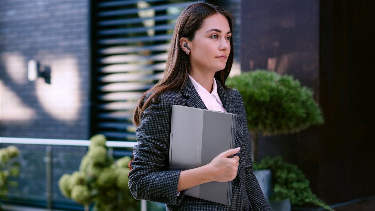 Woman wearing a fall business suit carrying a laptop computer under her arm as she walks down a city street .