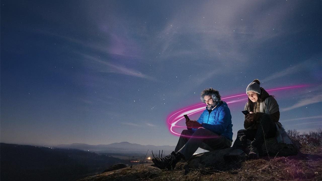 Pareja usando sus teléfonos de modelo sentados en una montaña a la luz de la luna.