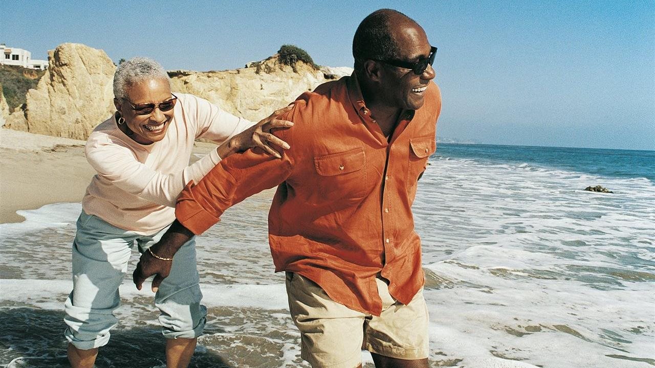 Senior couple enjoying the ocean spray and they walk along the beach.