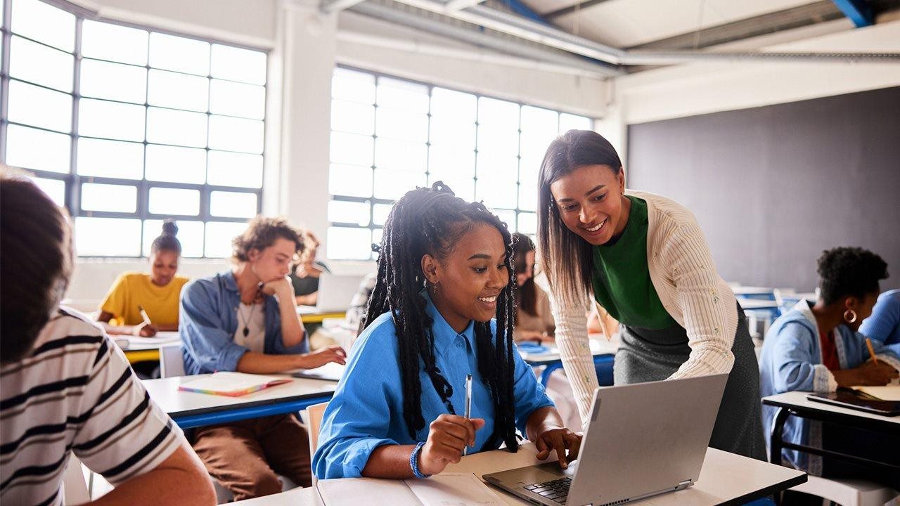 Teacher helping student in class while looking at a laptop computer.