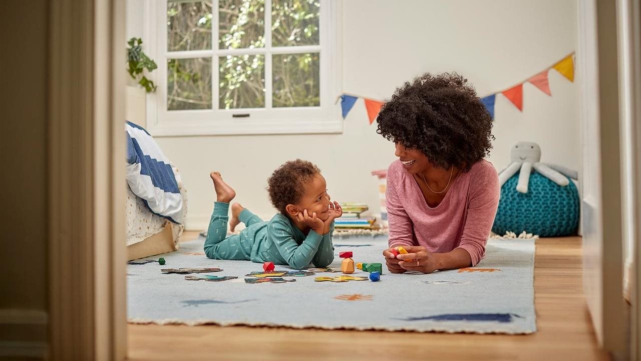 A mother and child lay on their stomachs playing in the child's bedroom.