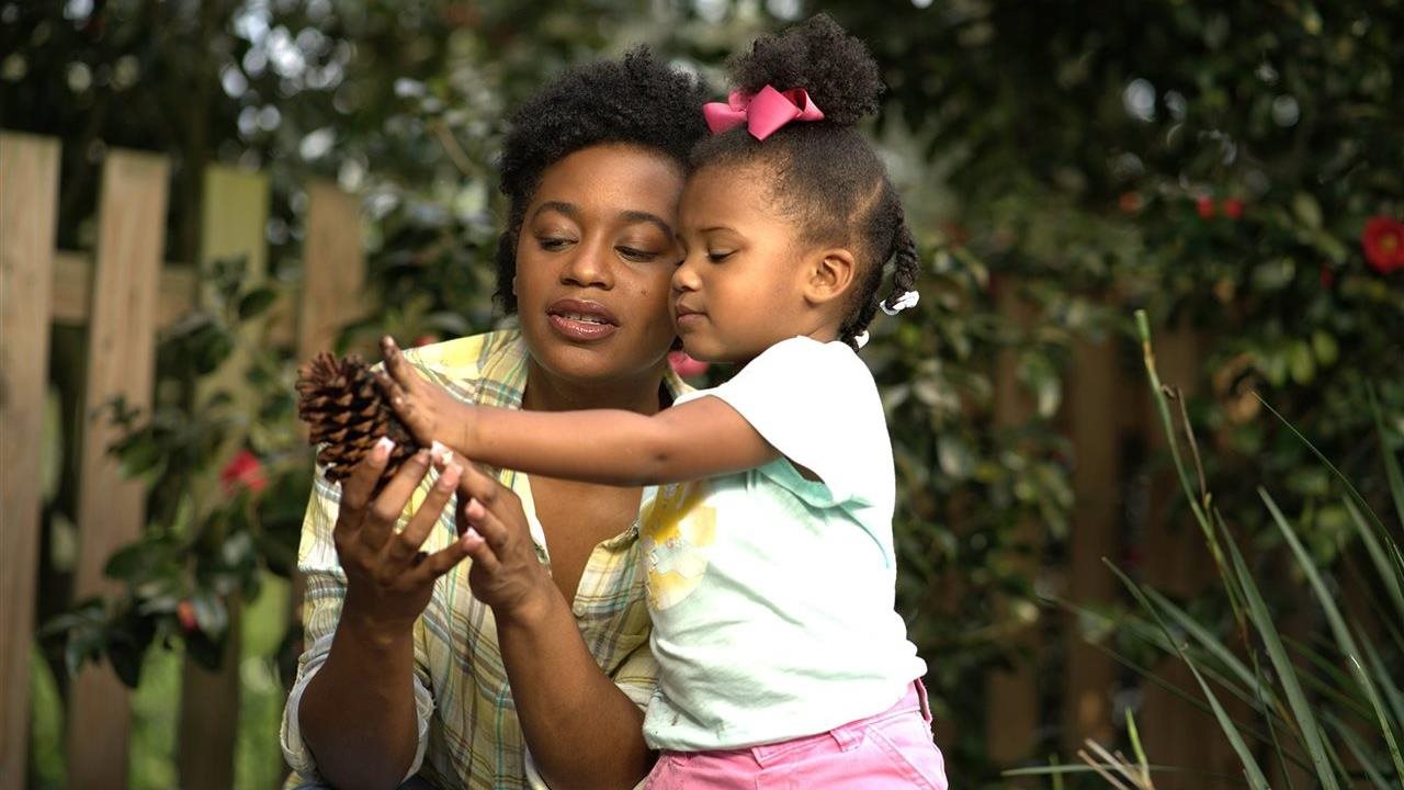 Mom and little girl looking at a pine cone while in the backyard.