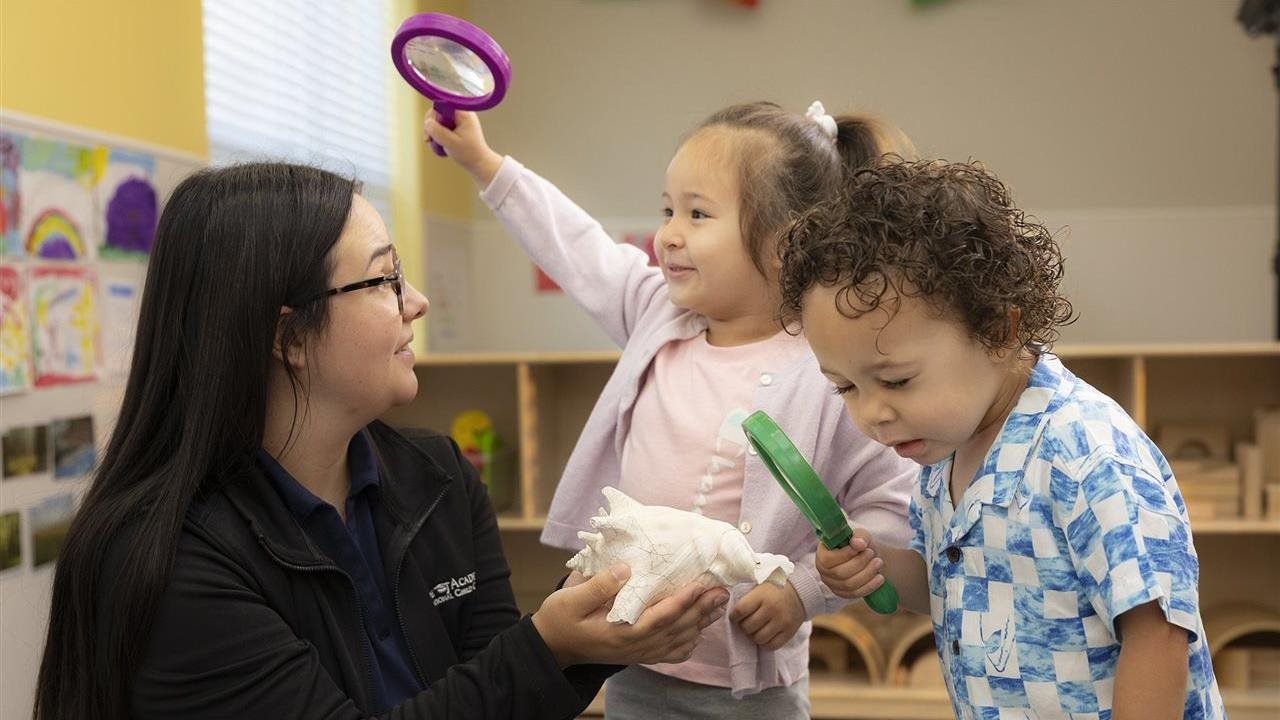 Instructor and two children playing with magnifying glasses at a Kiddie Academy® Educational Child Care Center.