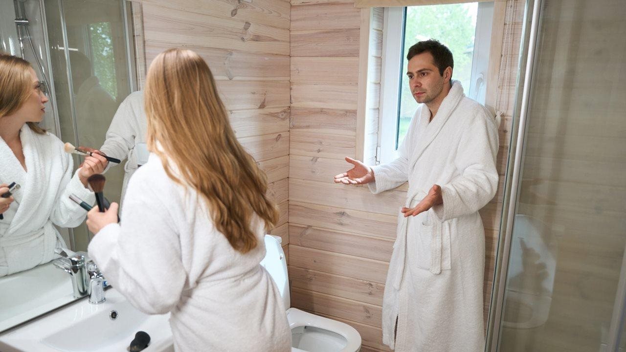 Couple wearing white terry robes trying to share a place at the sink in the bathroom.