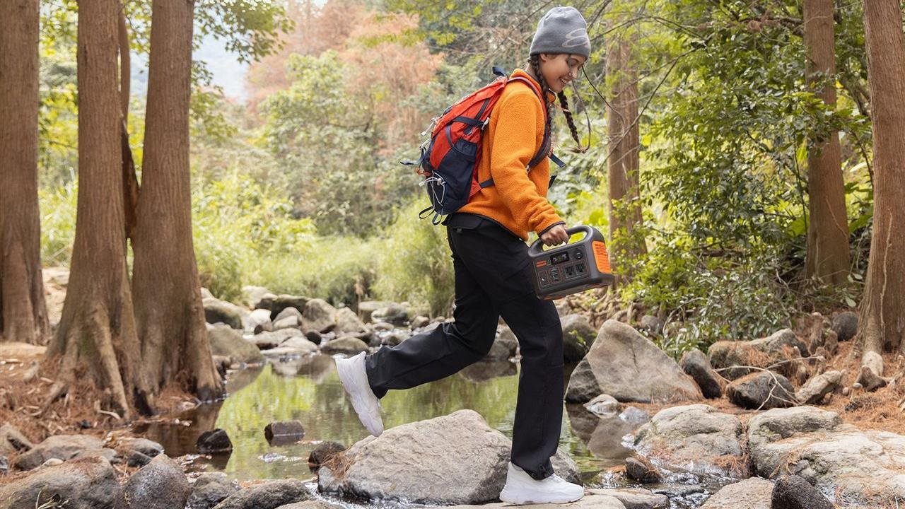 Woman hiking across rocks in a stream in the woods with The Jackery Explorer 300.