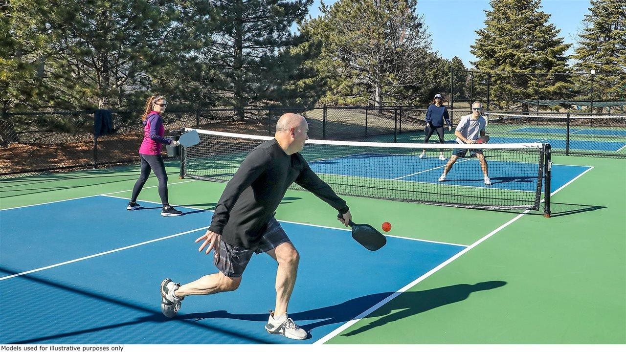 Older people playing pickle ball on a court in the summer.