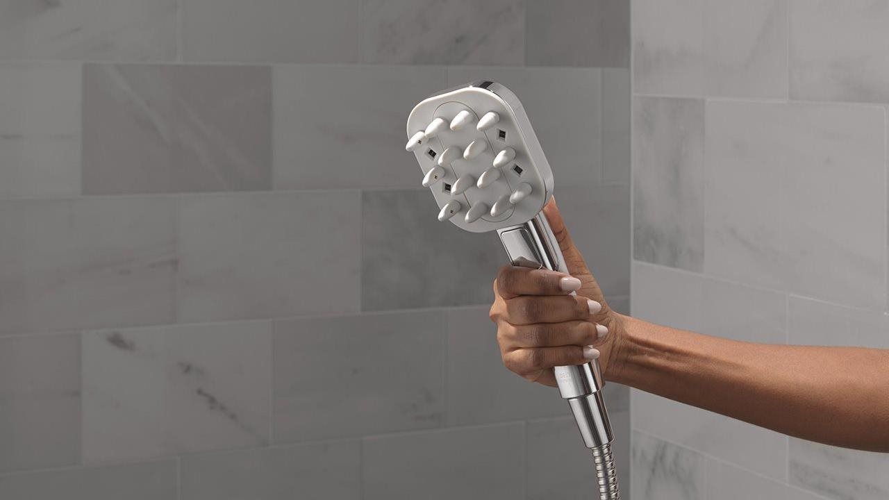 An arm holding a VersaCurl Tool in a gray stone shower
