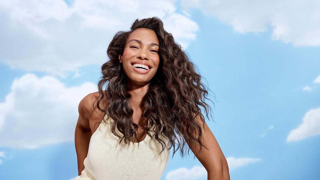 A woman smiles against a backdrop of clouds.