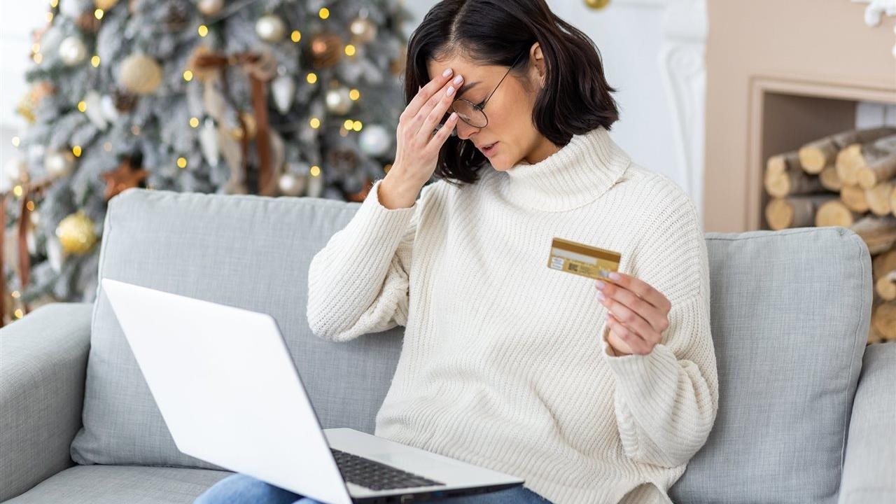 Woman sitting on a couch at home experiencing a cyber scam while holiday shopping online with credit card.