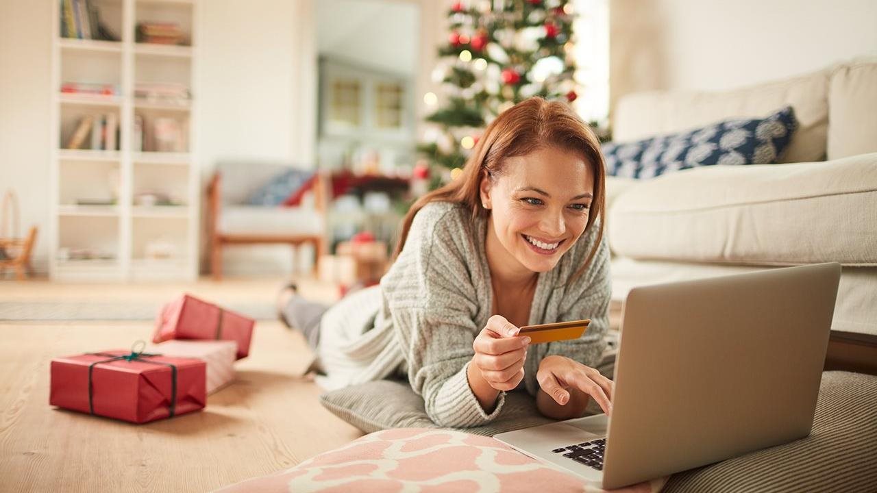 Woman laying on the floor in her festive living room using her laptop to shop for the holidays.