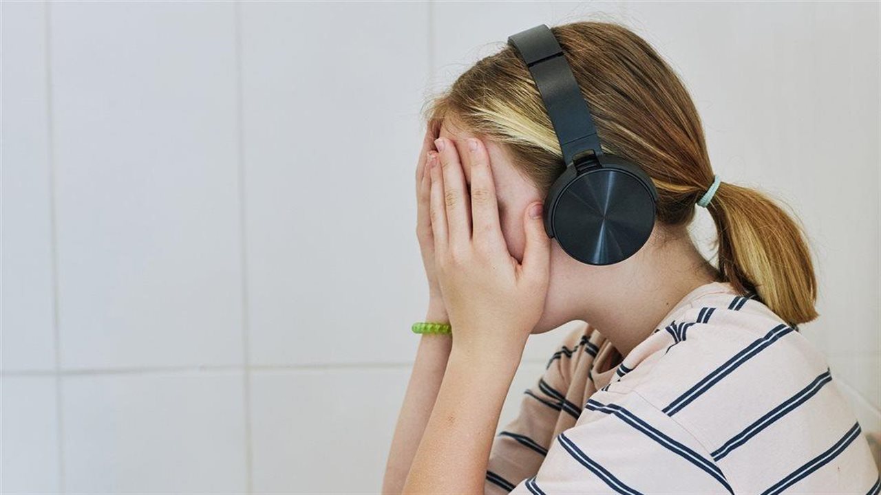 A young woman wearing headphones rests her head in her hands.