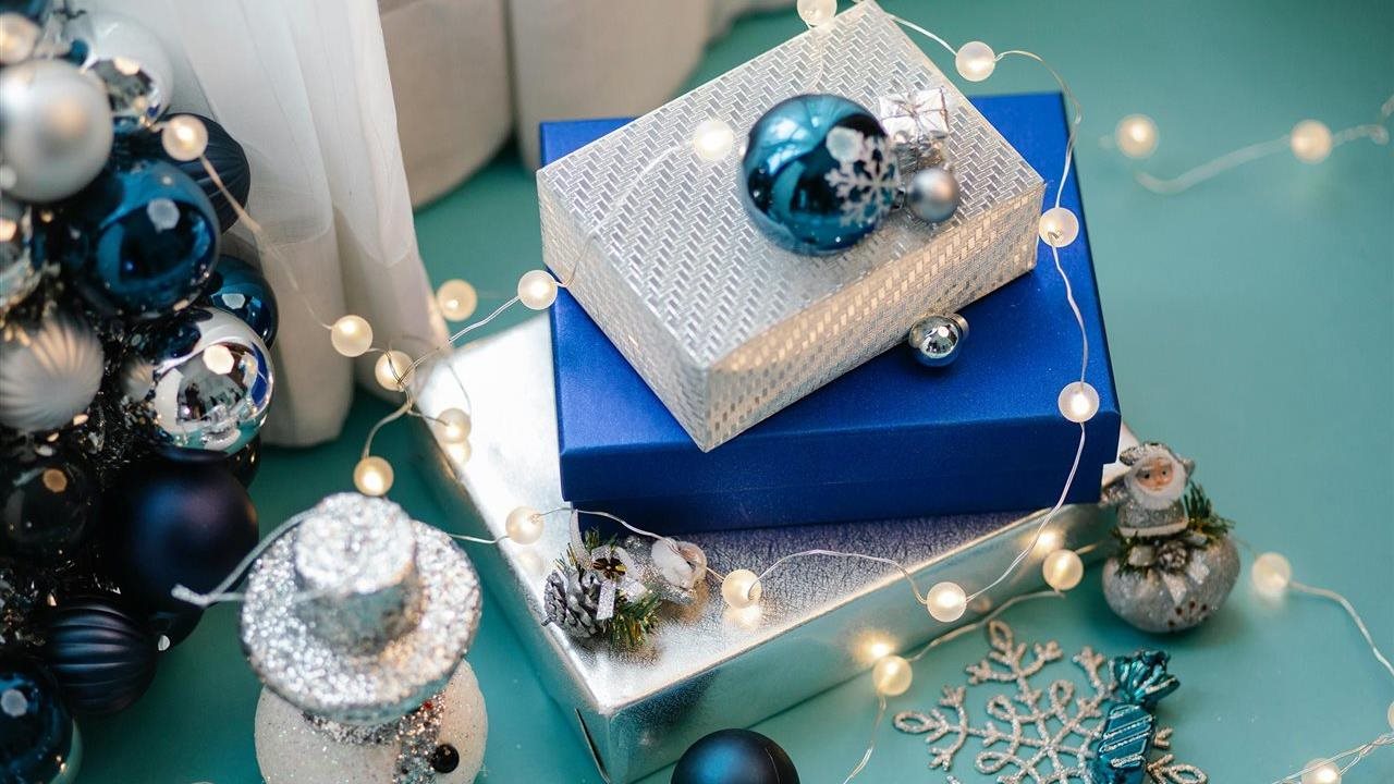 Holiday gifts wrapped in blue and silver paper next to a tree with blue and silver ornaments.
