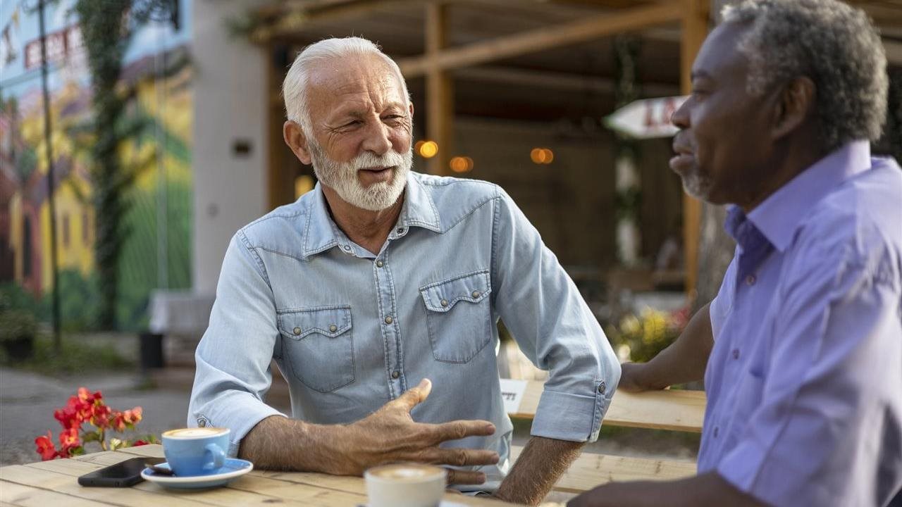 Two senior men talking outside over coffee. For more information and resources about bladder cancer, visit Merck.com.