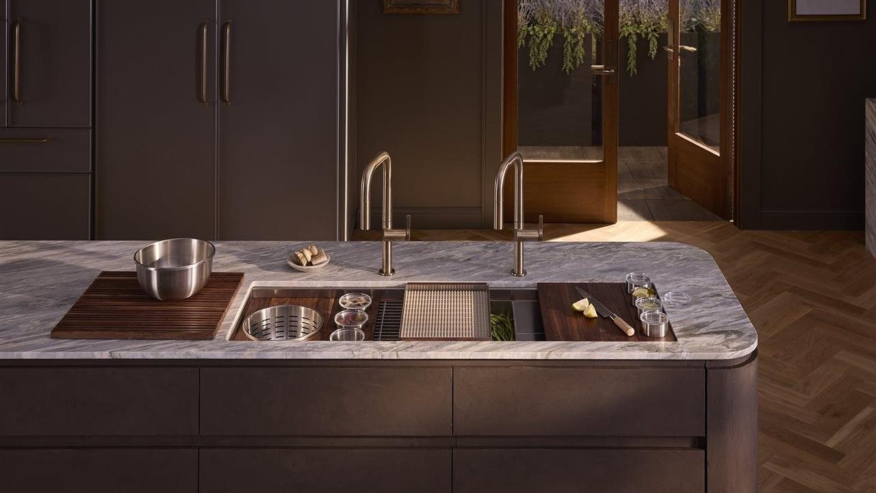 Upscale kitchen with a KOHLER® Synthos Workstation Sink that provides multi-functional accessories for prep, cooking and cleanup, including a solid wood cutting board, stainless steel colander, prep bowl set, garnish bowl set, durable sink rack, soaking bin, serving tray, pot rack, salad bowl set and sink cover.