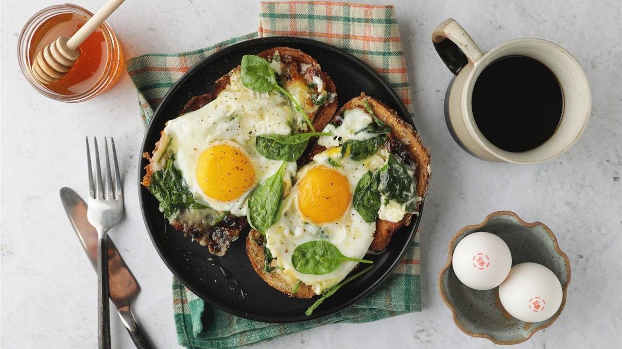 Hot honey toast with Eggland's Best eggs, toast and spinach on a plate next to coffee, honey and eggs on a table.