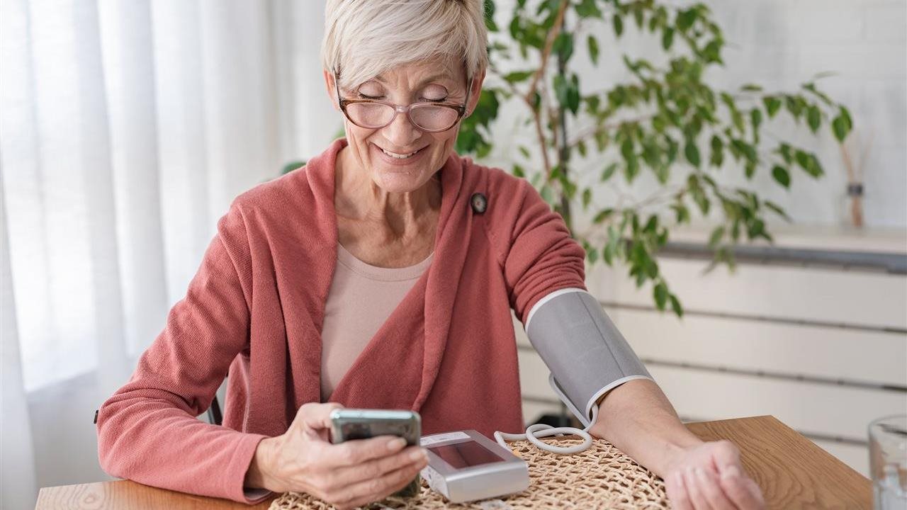 Senior woman takes blood pressure and uses phone app. Anthem Whole Health connects individual’s healthcare touchpoints.