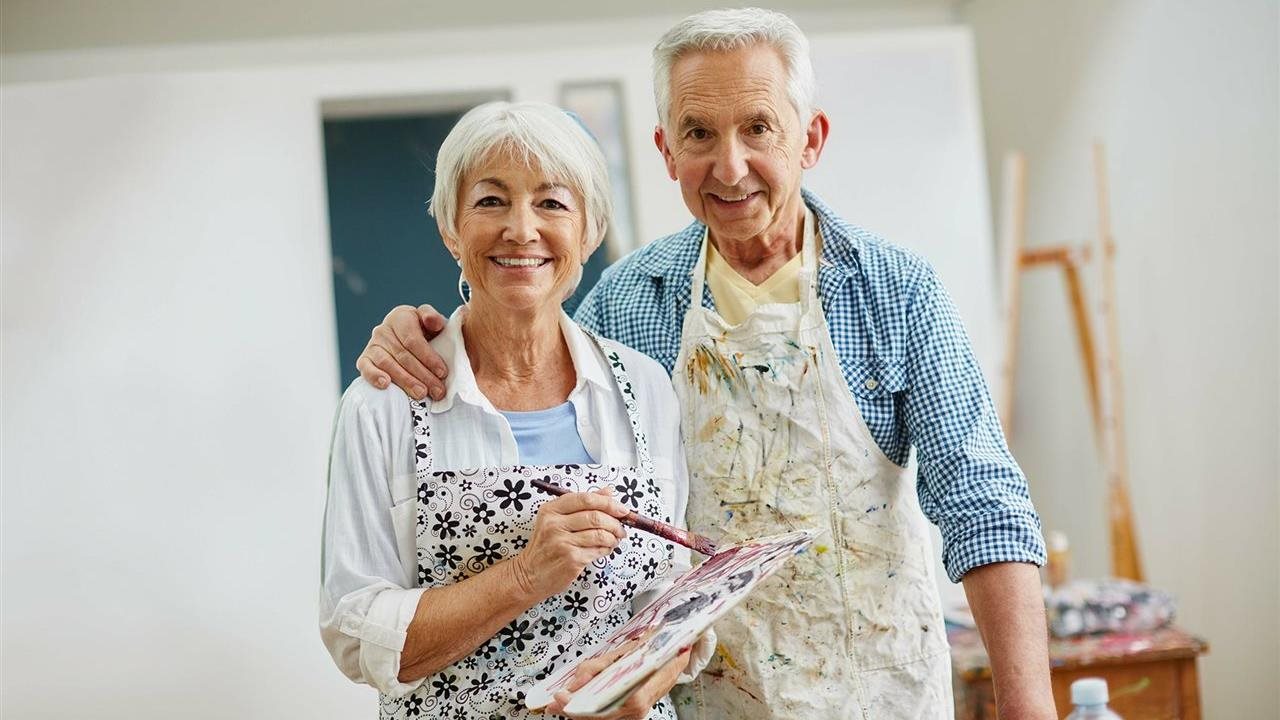 Older couple in painting aprons with paint palette enjoying their ability to paint following recommendations like the American Society of Retina Specialists (ASRS) recommendation to learn more about AMD to safeguard their vision.