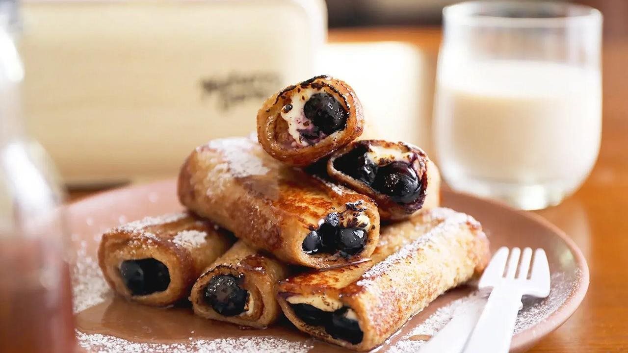 Blueberry Cream Cheese French Toast Roll-Ups made with Nature's Own Life Wheat + Protein Bread on a plate next to a glass of milk.