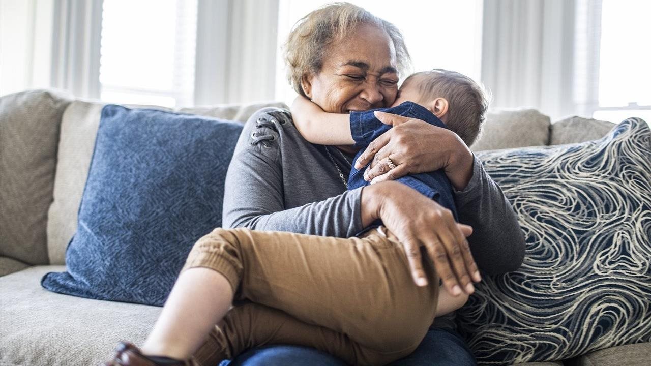 Grandmother gives grandson a hug while on the couch. UnitedHealthCare-UHC encourages families to celebrate grandparents.
