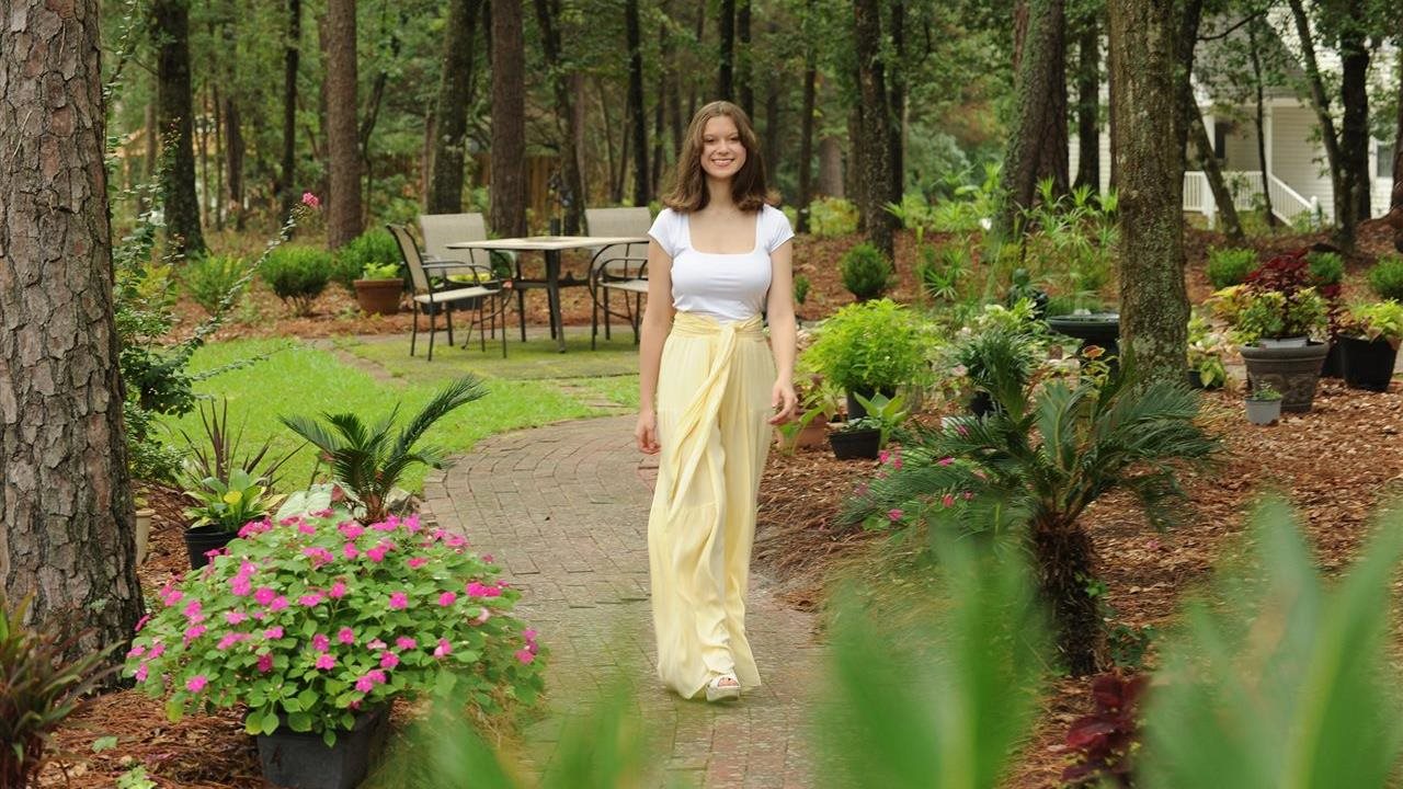 Sarah in a white and yellow dress walking on a path in a beautiful garden.