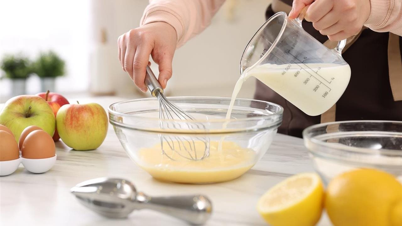 Woman in the kitchen pouring milk in to a bowl while making a recipe. Shelf-stable milk, thanks to a combination of ultra-high temperature (UHT) treatment and sterile aseptic packaging, can be stored at room temperature for months.