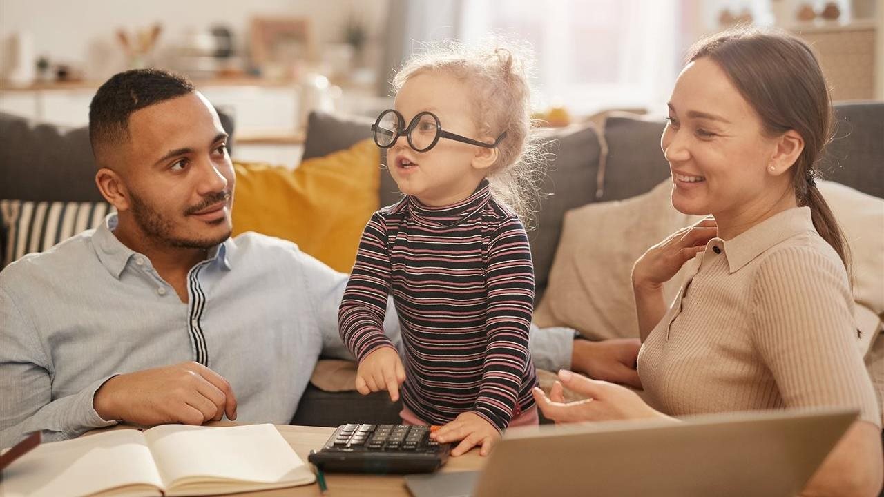 Adorable child wearing glasses upside down and pushing numbers on a calculator as his parents laugh.