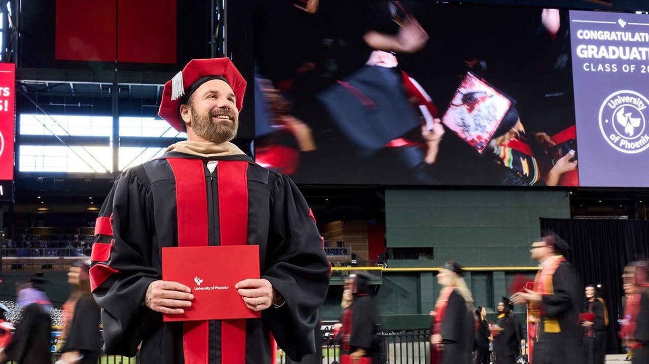 Smiling man at a University of Phoenix graduation ceremony holds his diploma.