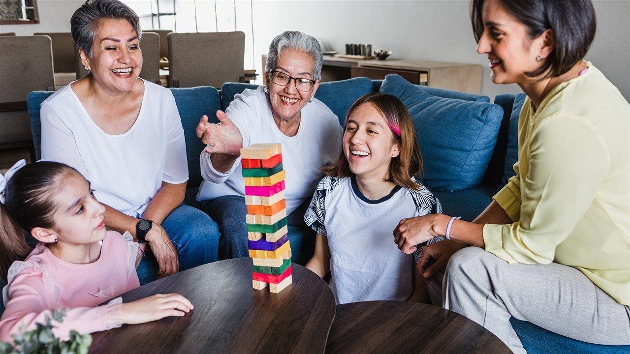 Cuatro generaciones de mujeres jugando al Jenga sobre una mesa de centro en el salón.