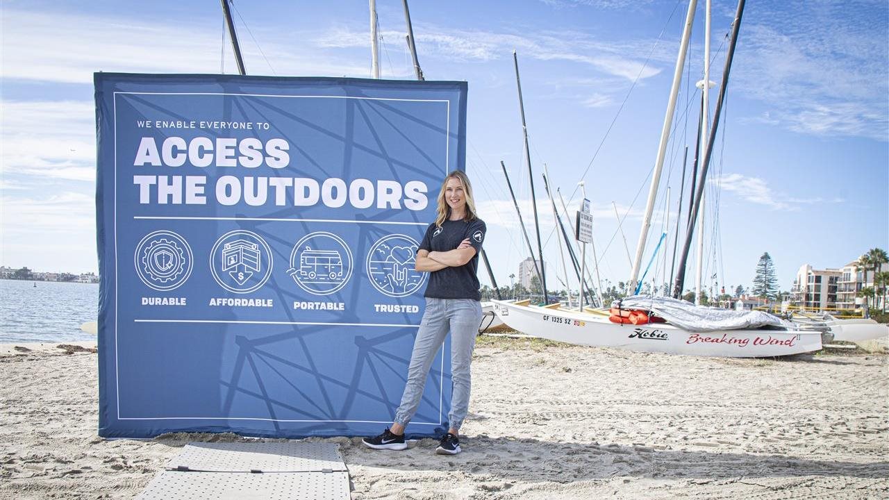 Woman standing on Acess Trax with a banner behind her that says "Access The Outdoors"