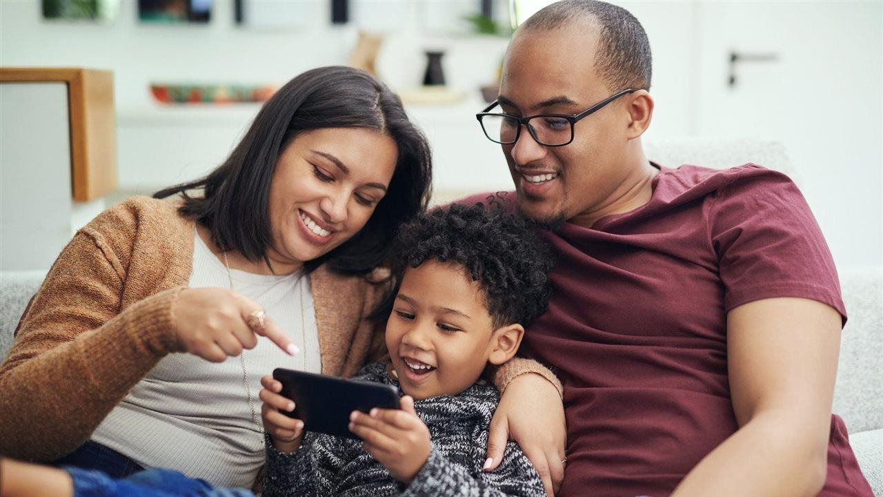 Una pareja y su hijo utilizando un teléfono celular en casa. Medicaid cubre a una amplia gama de familias e individuos.